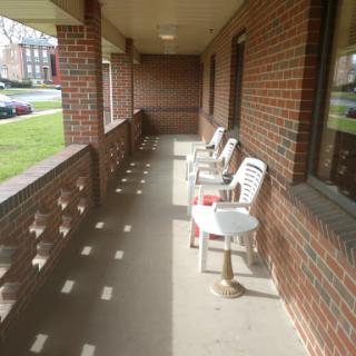 A quiet porch area featuring several plastic chairs and a view of the neighborhood.