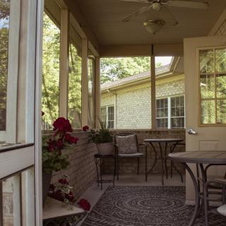 A cozy patio with outdoor seating and plants, illuminated by sunlight.