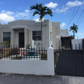A modern house with palm trees and gated entry under a cloudy sky.