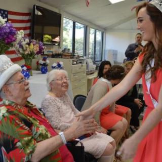 A cheerful interaction between a young woman in a sash and elderly individuals at an indoor event.