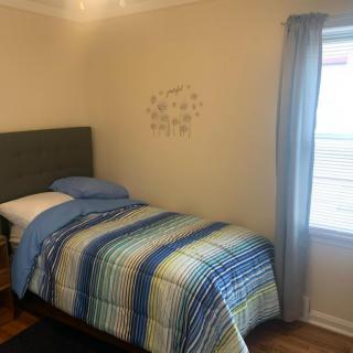 A cozy bedroom with a single bed featuring striped bedding, complemented by a nearby window with curtains.