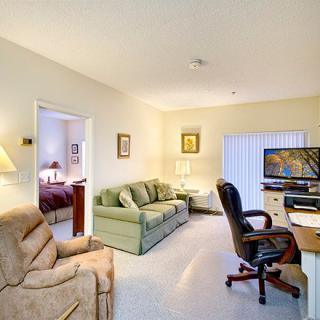 A cozy living room with a sofa, armchair, desk, and television.