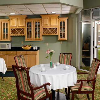 A cozy dining area with a round table set for four, featuring wooden cabinets and a microwave in the background.