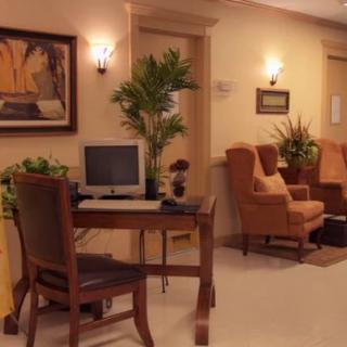 A cozy lobby area with a desk featuring a computer, surrounded by comfortable chairs and decorative plants.