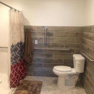 A bathroom with a toilet, shower, and tiled walls, featuring grab bars and a colorful shower curtain.