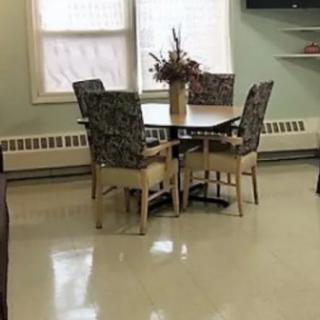 A dining area with a round table, chairs, and a flower vase by the window.