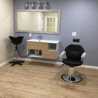 A modern salon setup featuring a styling chair, mirror, sink, and light fixtures.