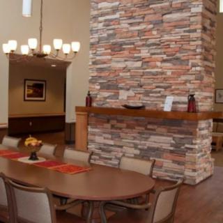 A modern dining room featuring a large stone fireplace, wooden table, and elegant chandelier.