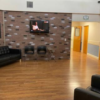 A modern waiting room with leather seating, a mounted TV, and a brick accent wall.