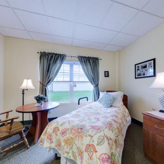 A cozy bedroom with a single bed, lamp, and window with curtains.