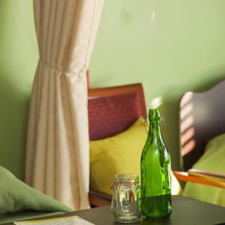 A cozy room with green walls, featuring a green bottle on the table, a chair, and a bed.