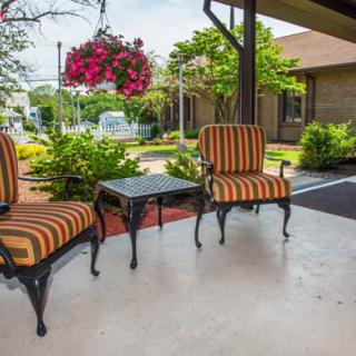 A cozy patio area with striped chairs and a small table, surrounded by a garden and hanging flowers.