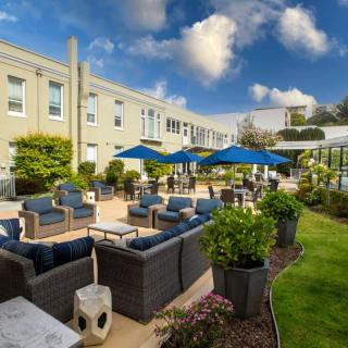 A beautiful outdoor patio area with comfortable seating and blue umbrellas, surrounded by well-maintained gardens.