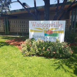 A sign for the Watsonville Nursing Center surrounded by greenery.