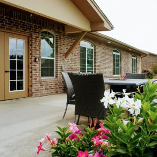 A cozy patio area with outdoor furniture and colorful flowers in front of a brick house.