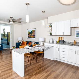 A modern open-concept kitchen and dining area with sleek white cabinets and wood flooring.