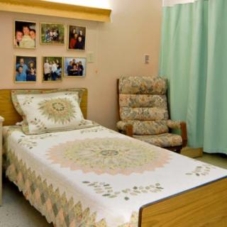 A cozy bedroom with a single bed, quilt, and decorative photographs on the wall.