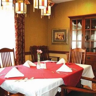 A cozy dining room featuring a table set with a red tablecloth and white napkins, surrounded by wooden chairs, illuminated by a chandelier.
