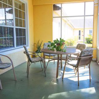A sunlit patio with a table and chairs, surrounded by yellow walls and plants.