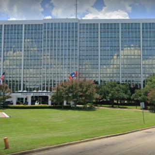 A large office building with a glass facade surrounded by a well-maintained lawn and trees.