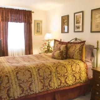 A cozy bedroom featuring a large bed with ornate pillows, framed artwork on the walls, and warm lighting.