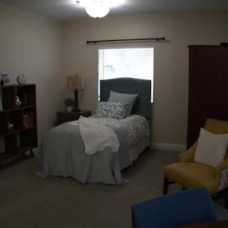 A cozy and well-decorated bedroom with a single bed, a reading chair, and a bookshelf.