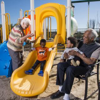 Children playing on a slide at the playground with adults supervising and enjoying the day.