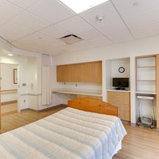A modern and clean hospital patient room equipped with a bed, storage, and a television.
