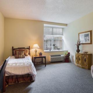 A cozy bedroom with a single bed, a warm lamp on a side table, and a window letting in natural light.