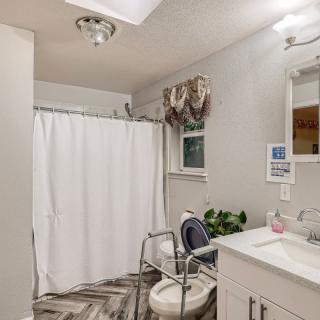 An accessible bathroom featuring a shower curtain, toilet safety frame, and a well-lit sink area.
