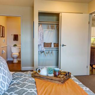A cozy bedroom features a neatly organized closet and an inviting tray on the bed, with a view into the adjoining bathroom.