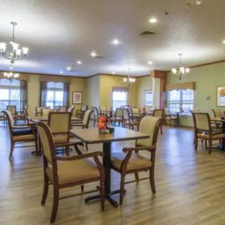 A spacious and well-lit dining area with multiple tables and chairs, featuring a wooden floor and large windows.