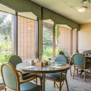 A cozy dining area in a restaurant with tables and chairs by large windows, allowing ample natural light.