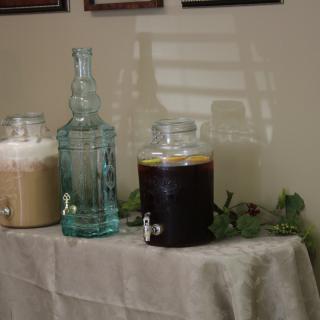 A table with glass beverage dispensers containing various drinks, set up indoors.