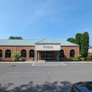 A brick building with a green metal roof, featuring arched windows and well-maintained landscaping.
