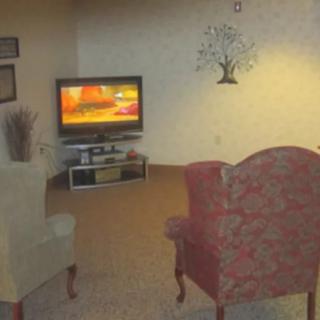 A cozy living room featuring a television, two chairs, and wall decor.