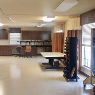 A well-lit modern workspace featuring a large table, ergonomic chair, and organized equipment storage.