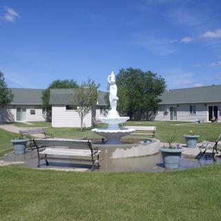 A courtyard with a central fountain surrounded by benches and grass.