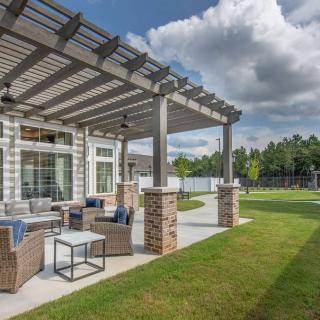 A beautiful outdoor patio with a pergola, furnished with comfortable seating, overlooks a lush lawn on a sunny day.