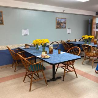 A cozy dining area with arranged tables and chairs, adorned with vases of yellow flowers.