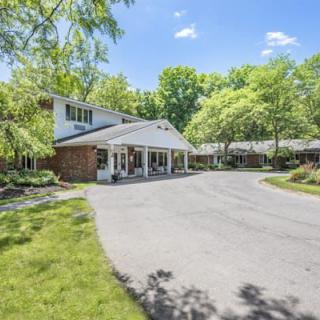 A picturesque view of a residential house with a spacious driveway lined by lush green trees.