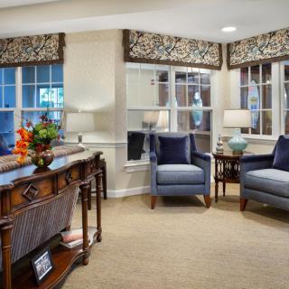 A cozy living room interior with elegant furnishings, including chairs, lamps, and large windows.