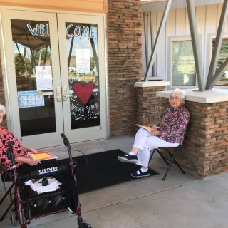 Two seniors seated outside a building entrance enjoying a sunny day.