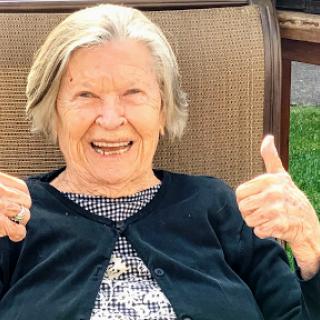 An elderly woman joyfully giving a thumbs up, showcasing her happiness.