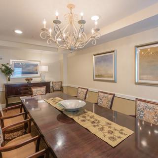 A spacious dining room featuring a large wooden table, elegant chandelier, and framed paintings on the walls.