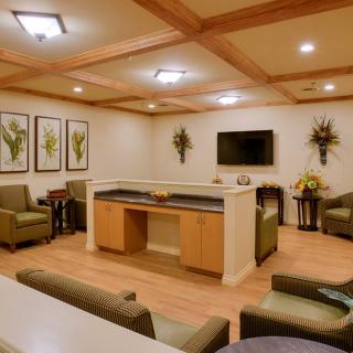 A cozy waiting room featuring comfortable seating, a wall-mounted television, decorative plants, and framed artwork.