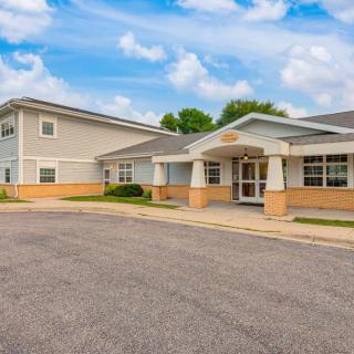A healthcare facility with a modern exterior design and an adjacent parking lot under a partly cloudy sky.