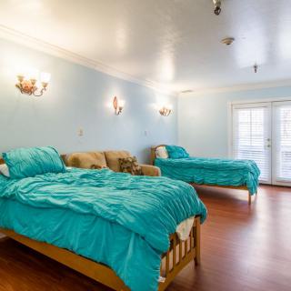 A bright bedroom with two turquoise-covered beds and a cozy couch.