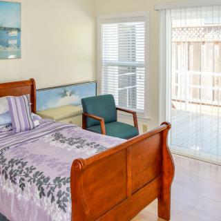 A cozy bedroom featuring a wooden bed, chair, and large windows with blinds.