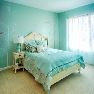 A cozy bedroom with turquoise walls and bedding, featuring a neatly made bed, a lamp on a nightstand, and sunlight streaming through the window.